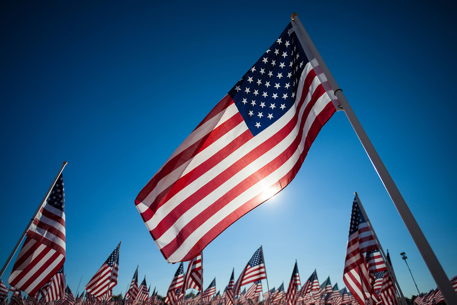 A display of many American flags with a sky blue background, com